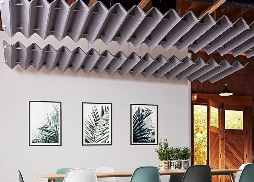 Acoustic panels suspended from a ceiling in a modern office space, above a dining table.