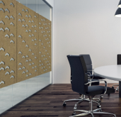 Office interior: wood-paneled wall with cut-out shapes, glass partition, round table, black chairs, wood floor.