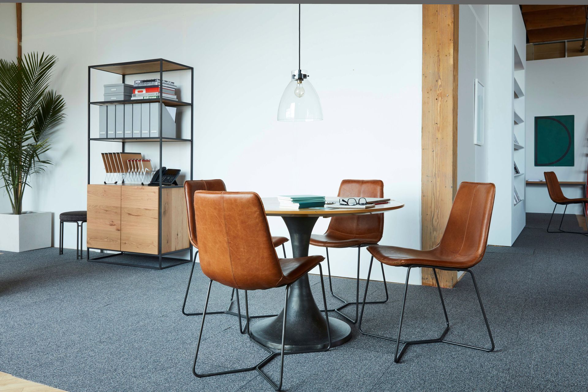 Dining area with round table, four brown leather chairs, shelving unit, and potted plant.