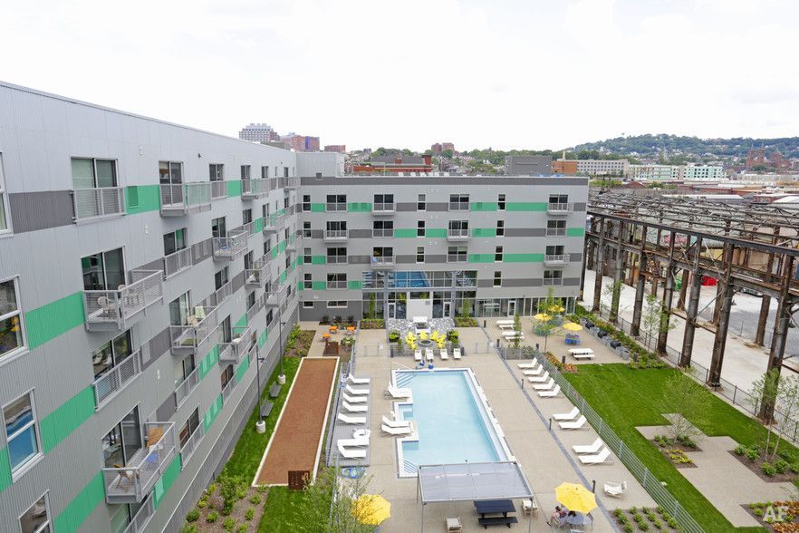 Apartment building with pool, lounge chairs, and greenery, in an urban setting.