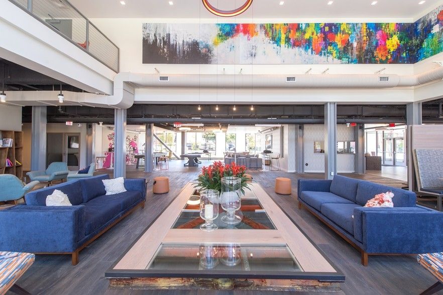 Modern lounge with blue sofas, large colorful artwork, and central coffee table.