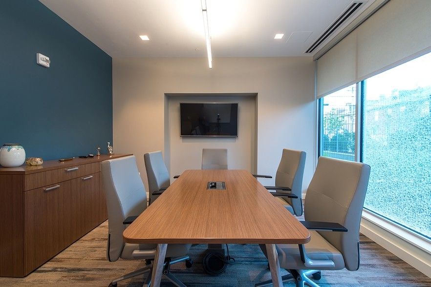 Conference room with wooden table, chairs, TV, and window with trees. Blue and beige walls.