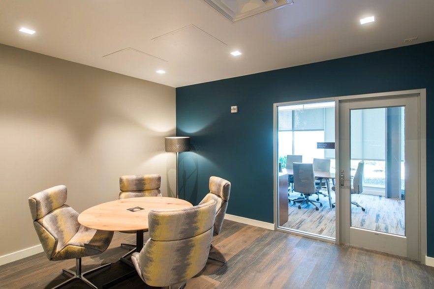 Conference room with round table and four patterned chairs, doorway to another room.