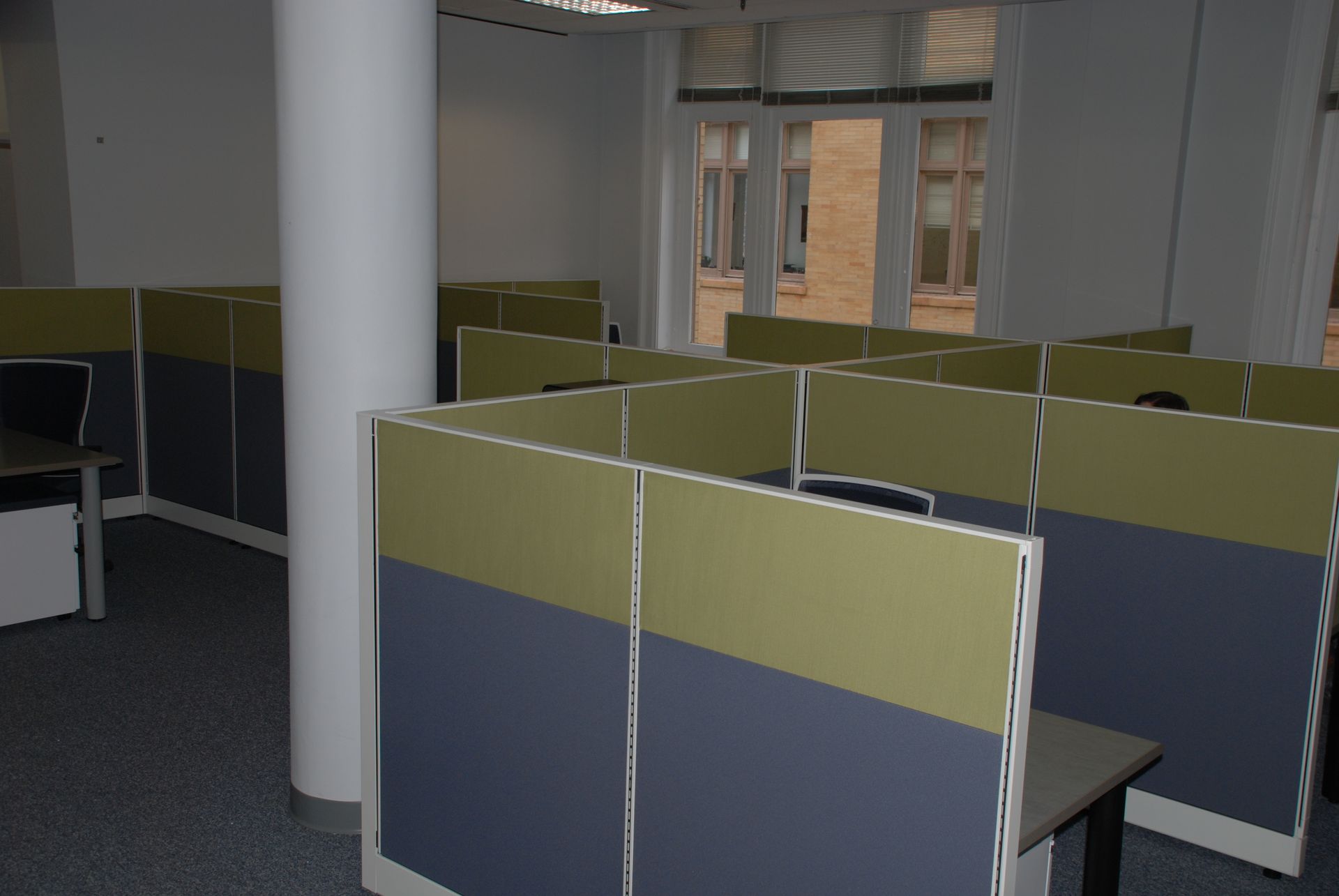 Empty office cubicles with two-tone gray/yellow dividers. A white pillar is in the center.