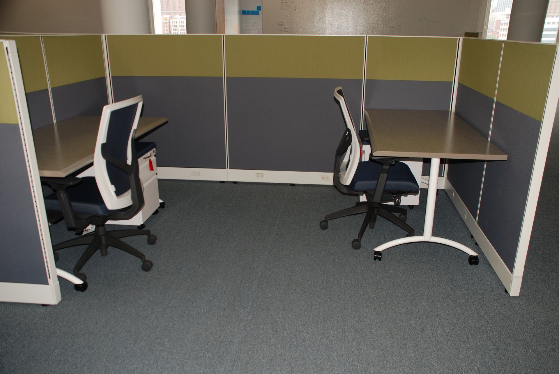 Two office cubicles with desks and chairs. Gray carpet.