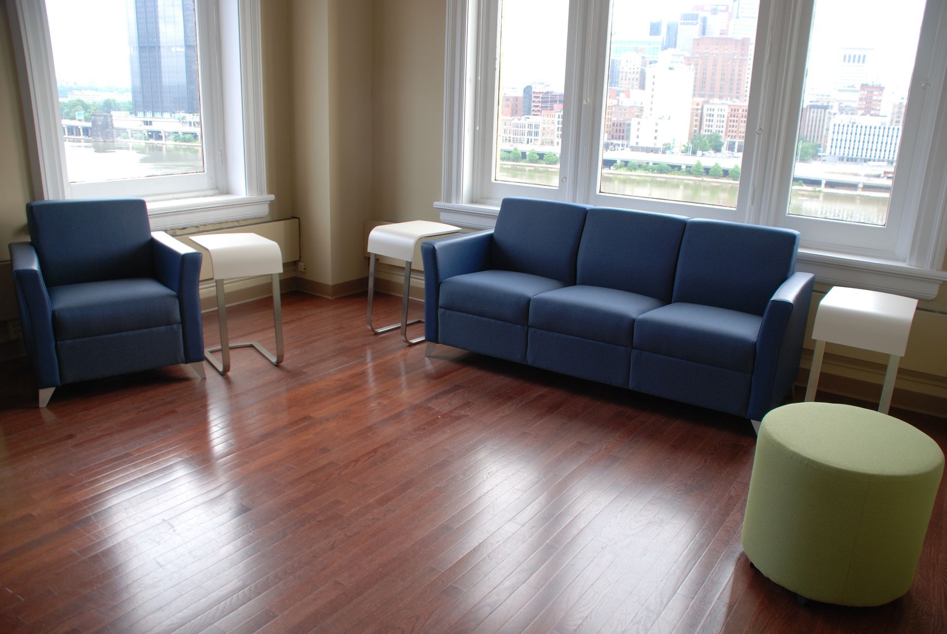 Blue sofa and armchair in a room with a cityscape view through large windows, hardwood floors.