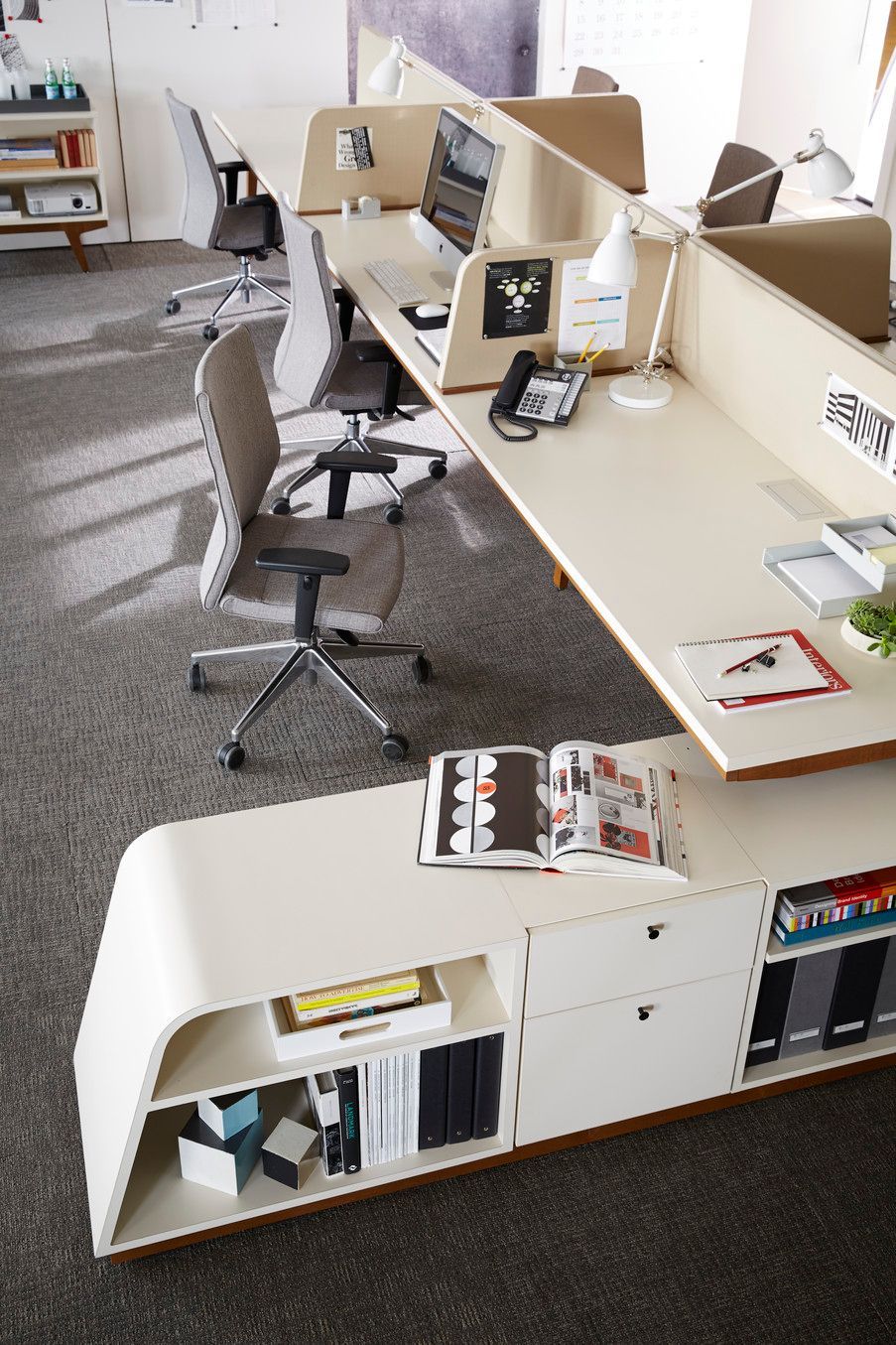 Modern office workspace with desks and storage, lit by natural light.
