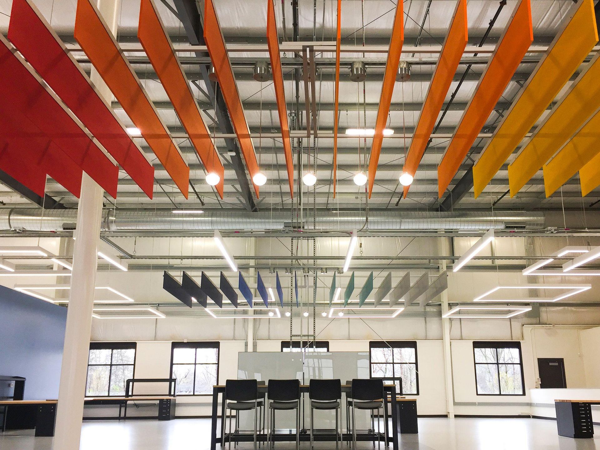Colorful office ceiling with orange, red, and yellow sound baffles, with a central workstation and windows.
