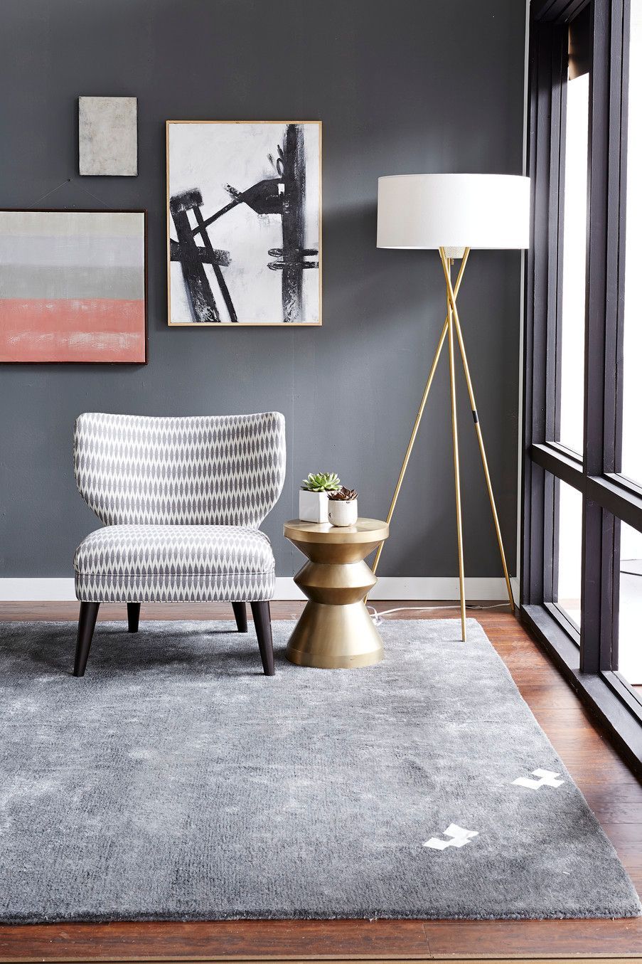 Cozy living room with gray walls, artwork, patterned chair, gold lamp, and a gray rug.