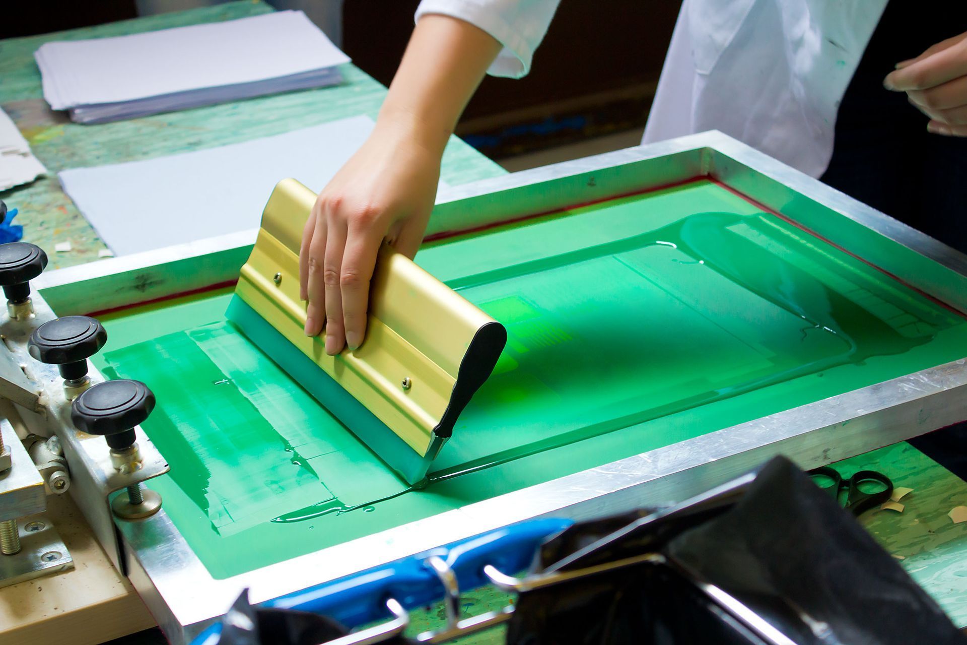 Person using a squeegee to apply green ink through a screen printing stencil.
