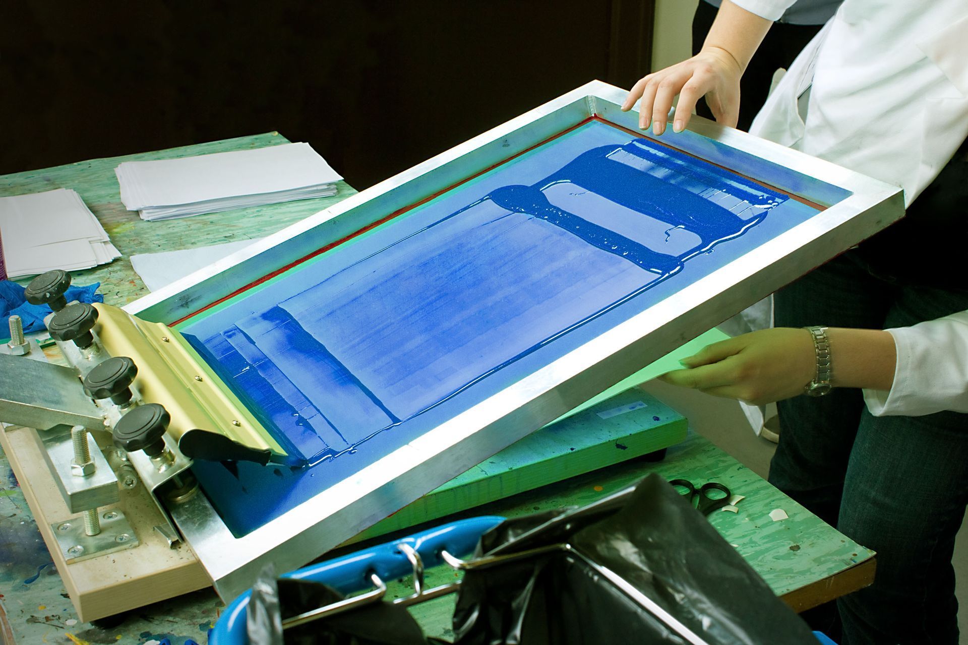 Person holding a screen printing frame with blue ink, preparing to print.