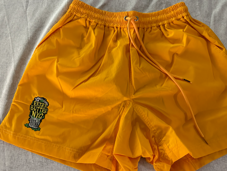Yellow shorts with a drawstring waist and a small graphic on the left leg.