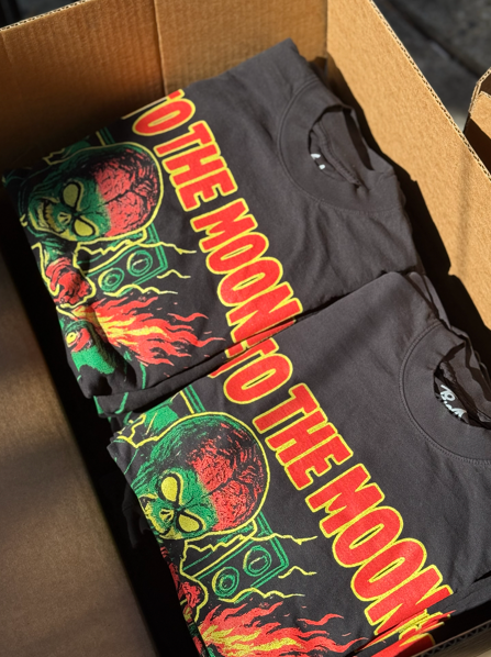 Two dark gray t-shirts folded in a cardboard box, with a colorful 