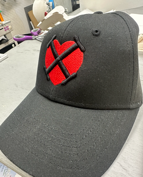 Black baseball cap with red heart and black cross, embroidered on the front.