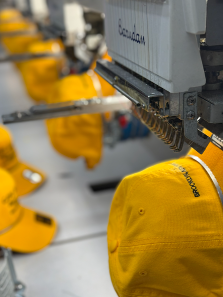Yellow baseball caps being embroidered by a multi-head industrial machine.