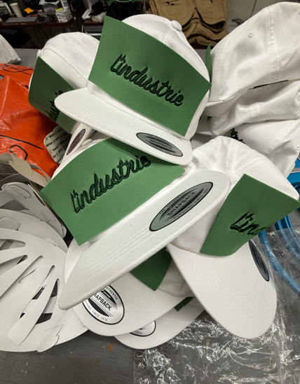 White and green Industrie logo caps piled together; some have a black curved bill.