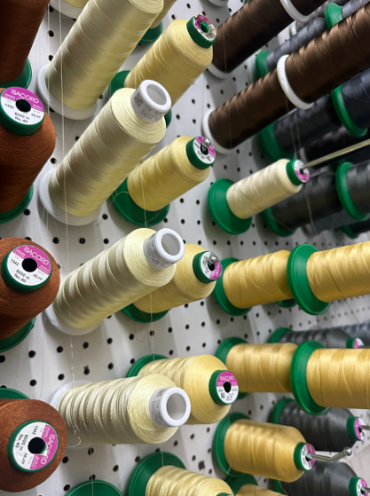 Spools of thread in various yellow, brown, and black colors mounted on a pegboard.