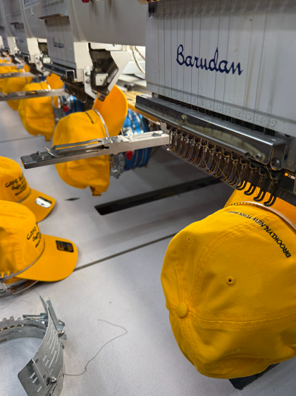 Yellow hats being embroidered by a row of industrial machines in a factory setting.