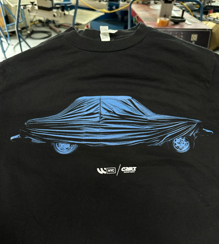 Black t-shirt with blue graphic of car covered in cloth. 