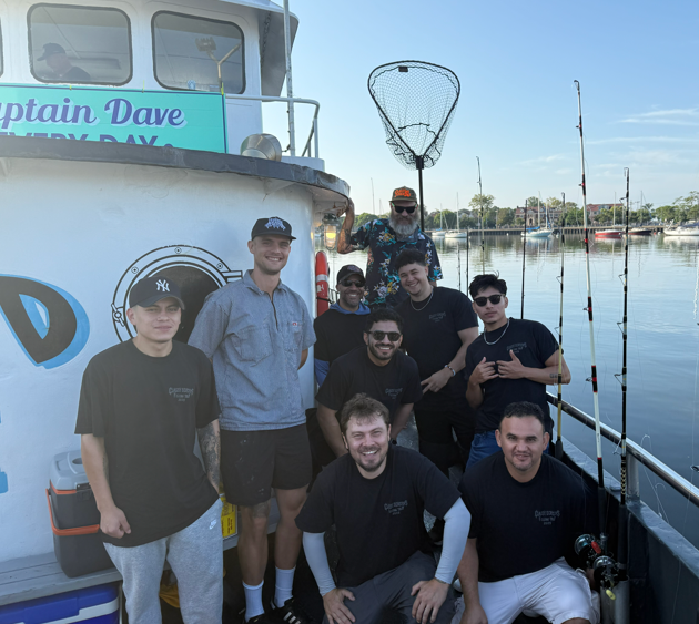 Group of people on a boat, posing for a photo. A man is holding a net. 