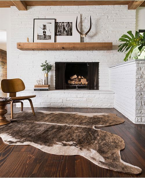 White brick fireplace with wooden mantel, brown cowhide rug on dark wood floor.