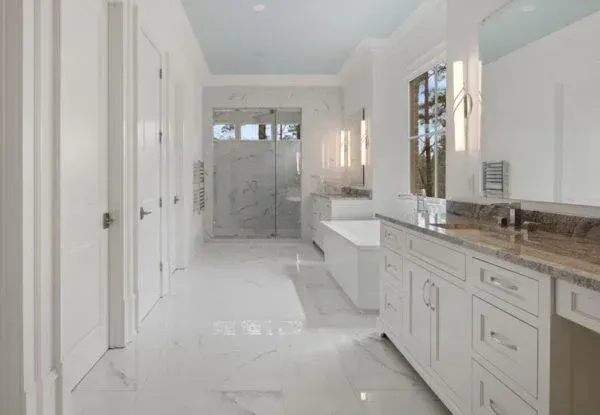 Spacious white bathroom with marble floor, large vanity, tub, and glass shower.