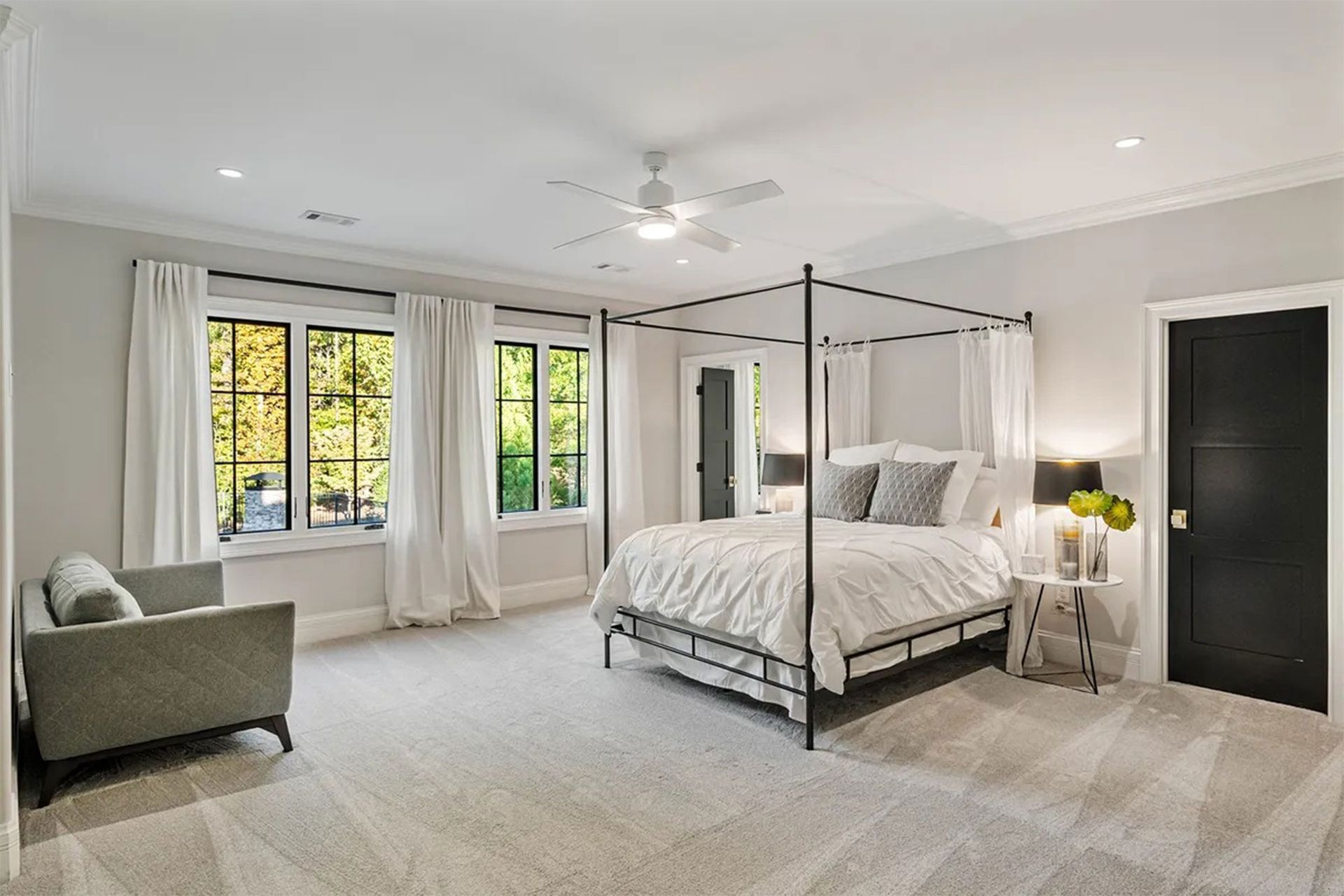 Bedroom with canopy bed, gray walls, white drapes, sofa, and a black door.