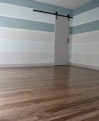 Empty room with hardwood floors, horizontal blue and white striped walls, and a sliding barn door.