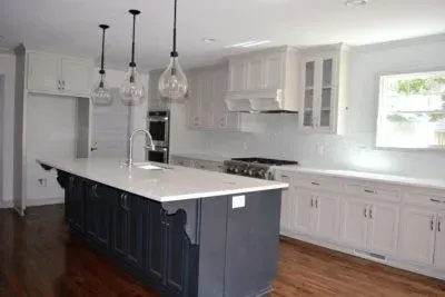 Modern kitchen with white countertops and cabinets, dark blue island, pendant lights, and stainless steel appliances.