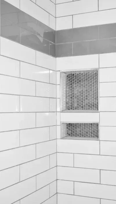 White tiled shower corner with two built-in storage niches and a gray band of tiles.