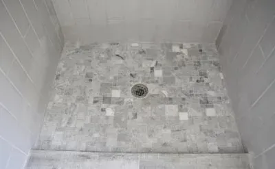 Shower stall with grey marble tiled floor and walls; central drain.
