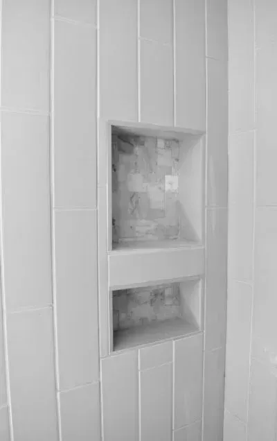 Recessed tiled shower niche with two shelves, installed in a white tiled wall.