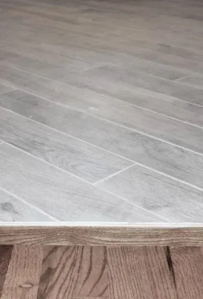 Herringbone gray tile flooring meets brown wood flooring, with a visible edge.