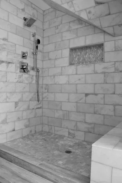 Shower with white tile walls and floor, recessed shelf with mosaic tile.