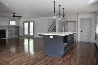 Open-concept kitchen and living area with a dark gray island, hardwood floors, and white walls.