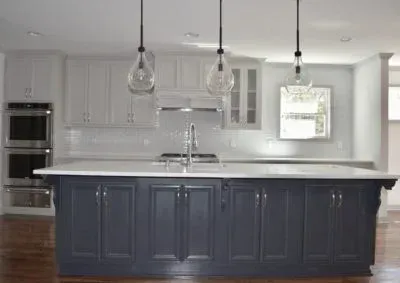 Kitchen with gray island, white countertops, and light fixtures. White upper cabinets, stainless steel appliances.