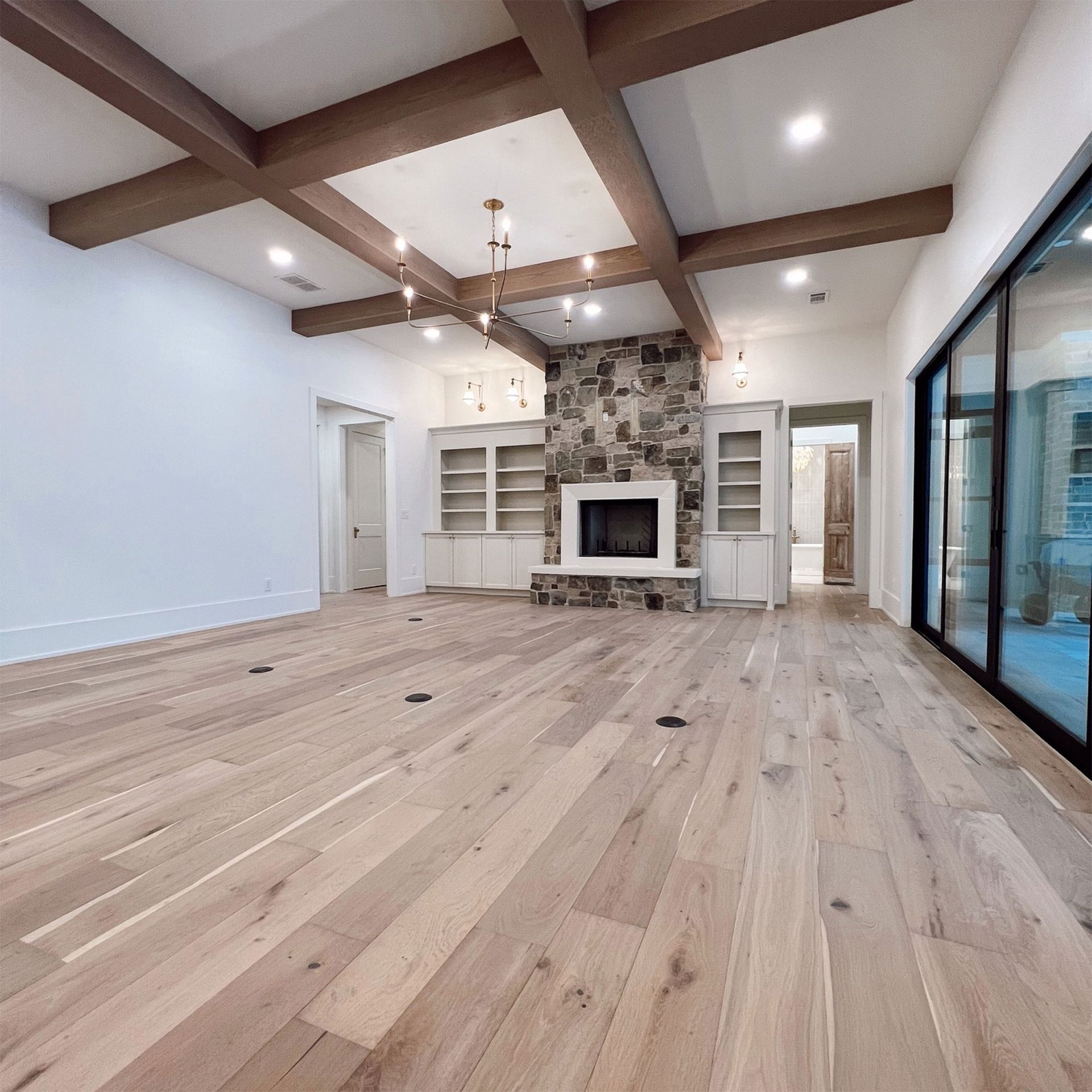 Spacious living room with wood floors, stone fireplace, built-in shelving, and large windows.
