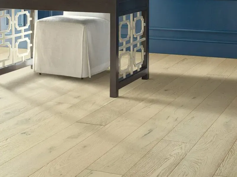 Wooden floor with light brown planks, under a dark desk with decorative side panels, a white chair, and blue wall.