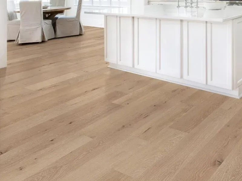 Light wood floor in a kitchen with a white island and dining area in the background.