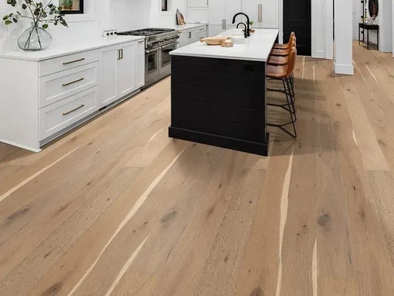 Light wood flooring in a modern kitchen with white cabinets, black island, and bar stools.