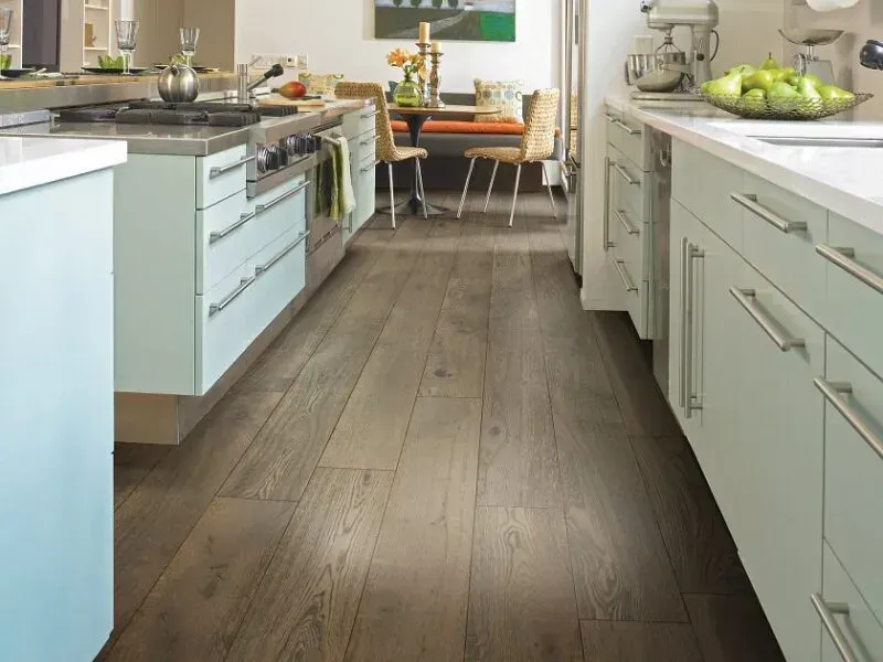 Kitchen with light blue cabinets, stainless steel stove, and wood flooring. A dining area is visible in the background.