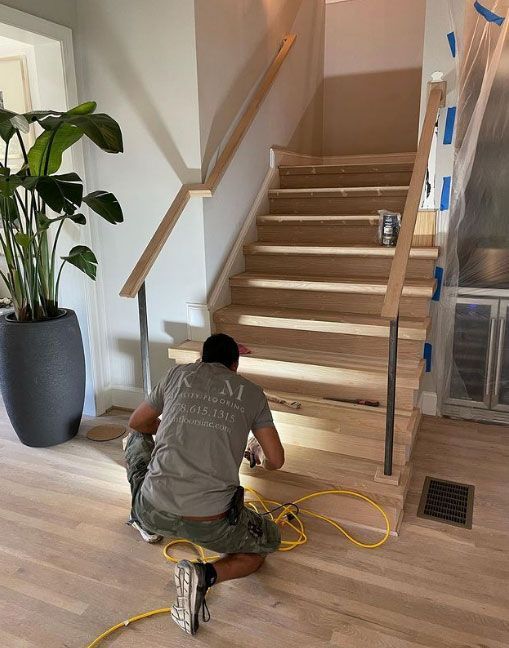 Man installing stairwell with wooden steps and railing. He is kneeling near the bottom.