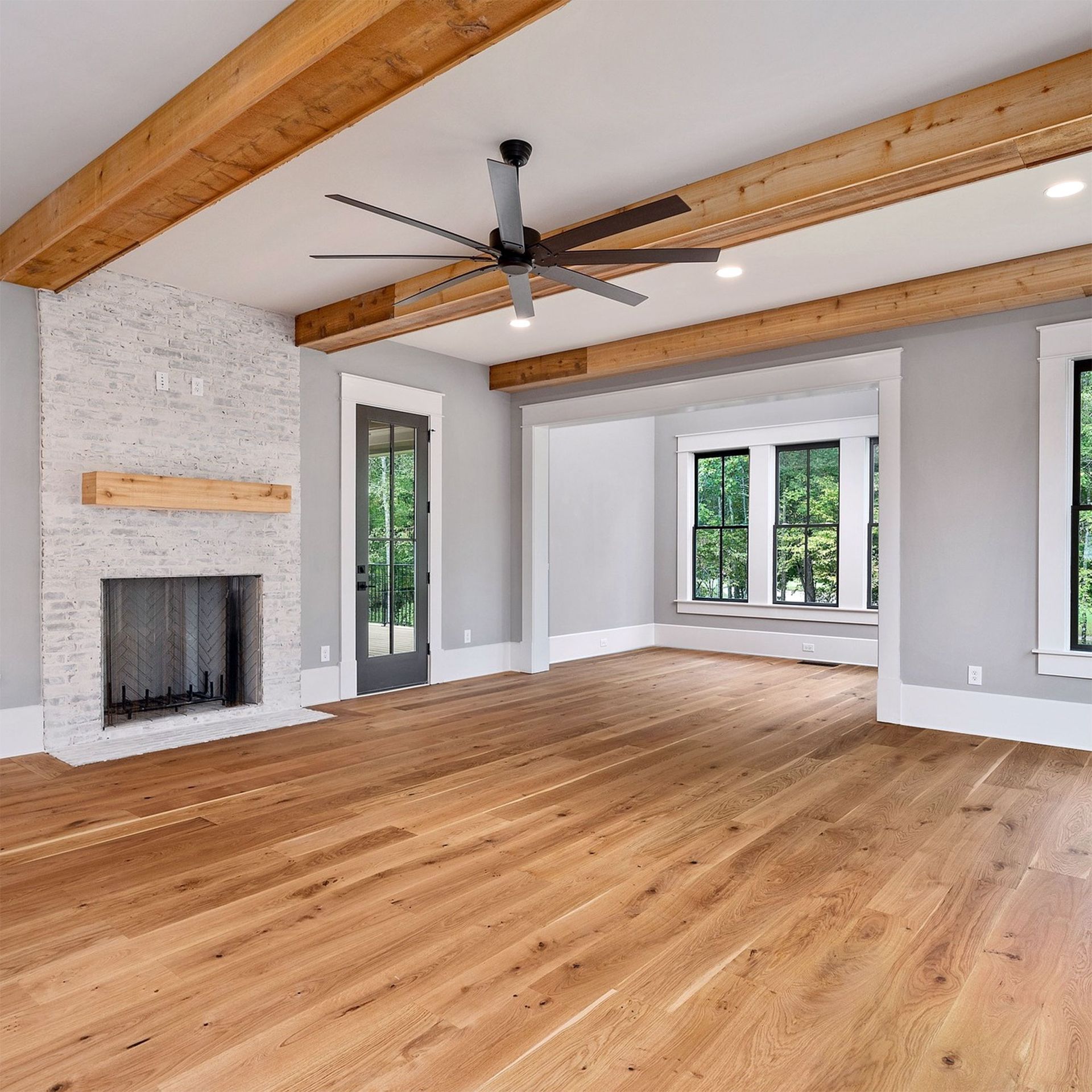 Empty room with hardwood floors, a fireplace, exposed wooden beams, and a ceiling fan.