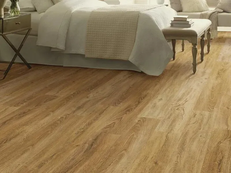 Bedroom with light wood-look flooring. A bed with white linens and a bench are in the room.