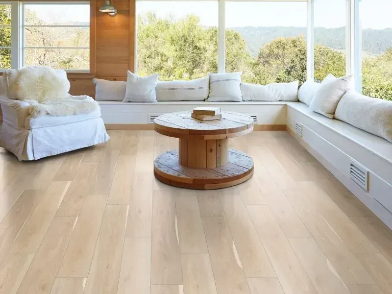 Light wood-floored sunroom with large windows, white seating, and a round wooden coffee table.