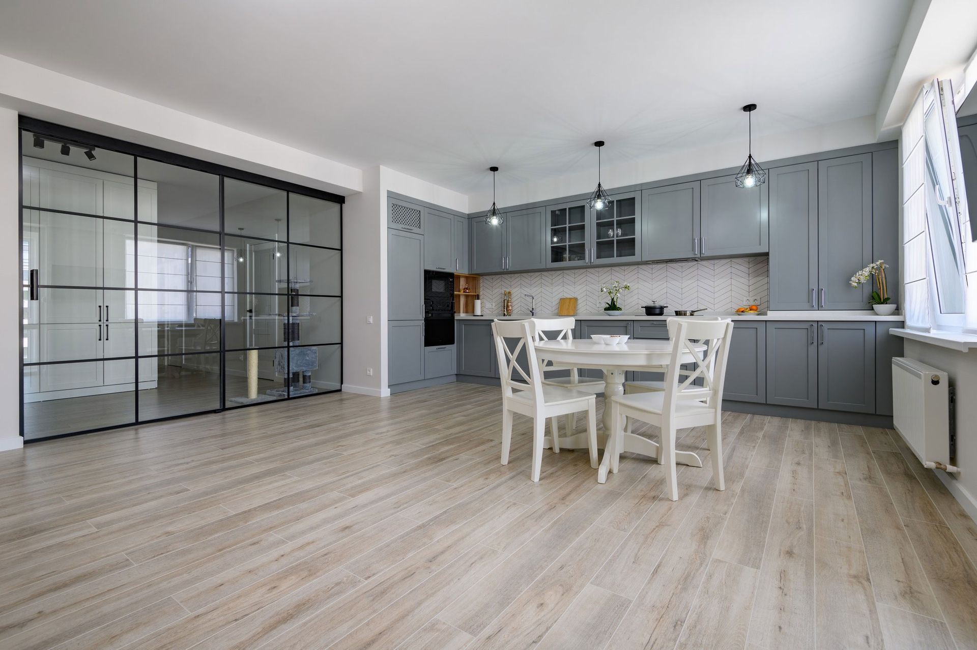 Modern kitchen with grey cabinets, white table, chairs, and glass sliding doors.
