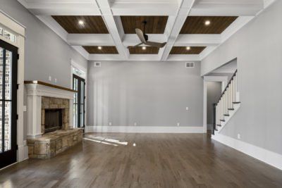 Spacious living room with fireplace, wood floor, coffered ceiling, and stairs leading up.