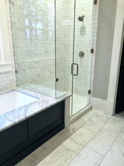 Bathroom with a glass shower, marble tile, and a dark-colored tub.