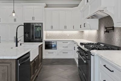 White kitchen with dark appliances, cabinets, and a farmhouse sink. Light-colored countertops and gray flooring.