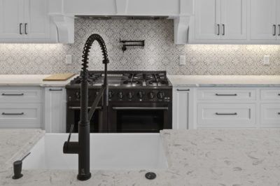 Black faucet and range in a white kitchen with decorative tile backsplash.